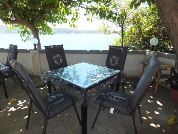 An outdoor patio with a glass table and black metal chairs, overlooking a body of water.