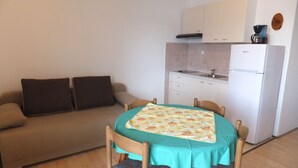 En kompakt opholdsstue med et tekøkken, et spisebord med stole og en sofa med puder.