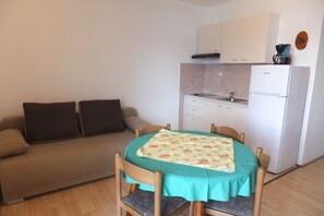 A compact living space with a kitchenette, a dining table with chairs, and a sofa with cushions.