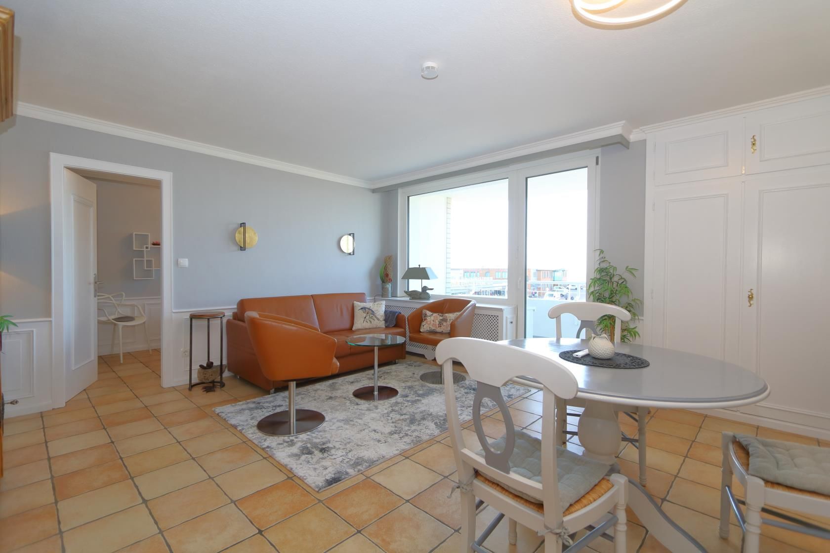 A modern living room with a sofa, chairs, a dining table, and a view through large windows.