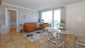 En moderne stue med sofa, stole, spisebord og udsigt gennem store vinduer.