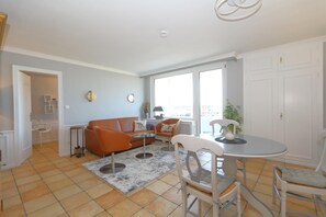 Een moderne woonkamer met een bank, fauteuils, een eettafel en uitzicht op de stad door grote ramen.