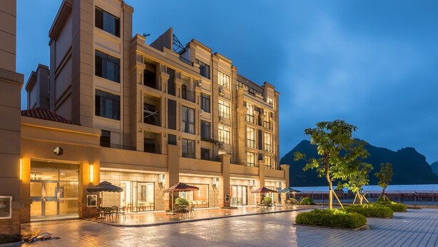 A multi-story hotel with a courtyard, outdoor seating, and a mountain backdrop. - Meeteem Boutique Hotel (Baise)