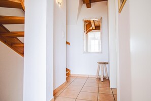 Een smalle gang met een houten plafond, een klein krukje en een raam.