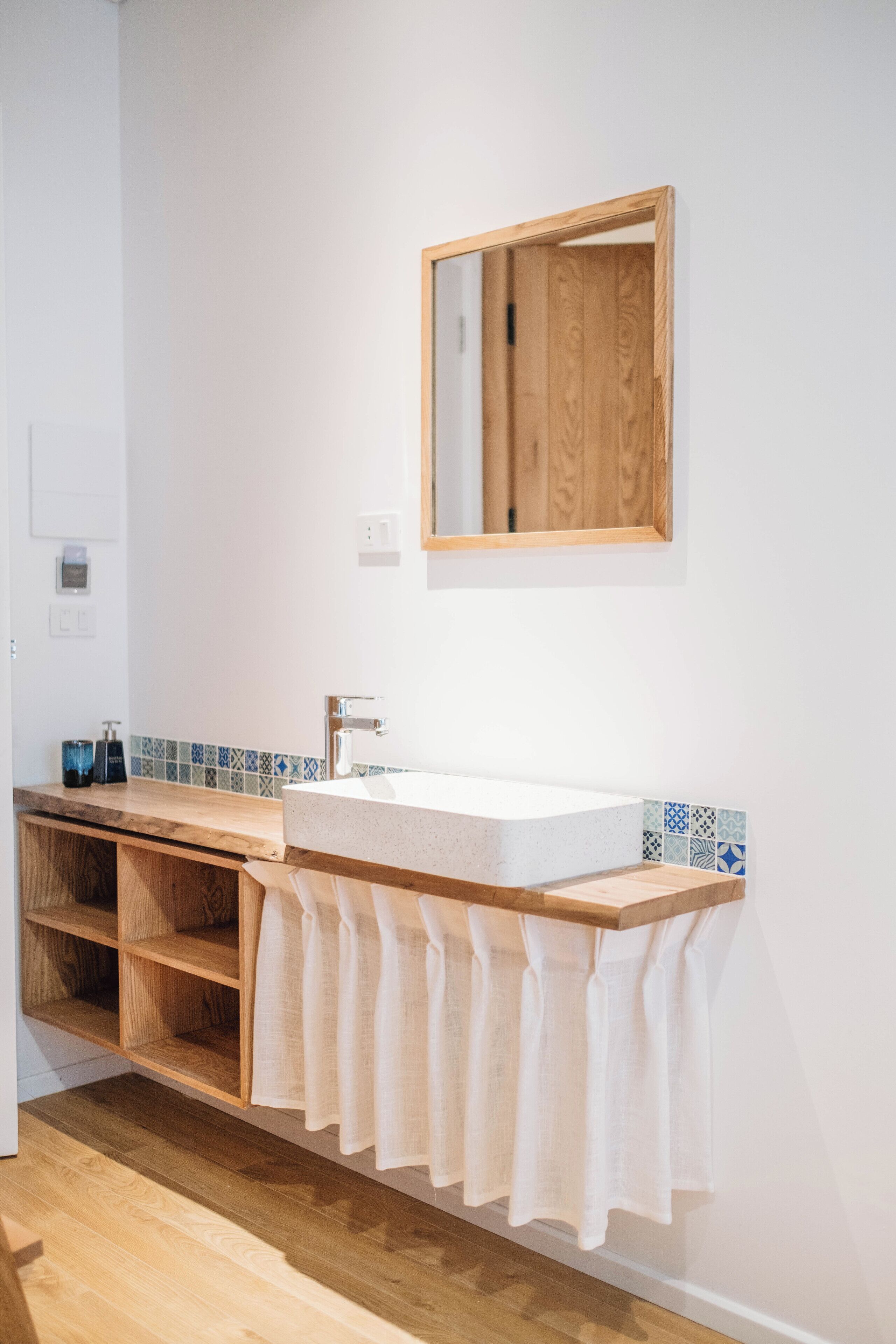 Ein Badezimmer mit einem Holzbadezimmerhocker, einem weißen Waschbecken und einem Spiegel.