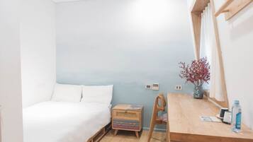 Une chambre à coucher comprenant un lit, une table de chevet en bois, un bureau, une chaise, un miroir et une fenêtre avec des rideaux.