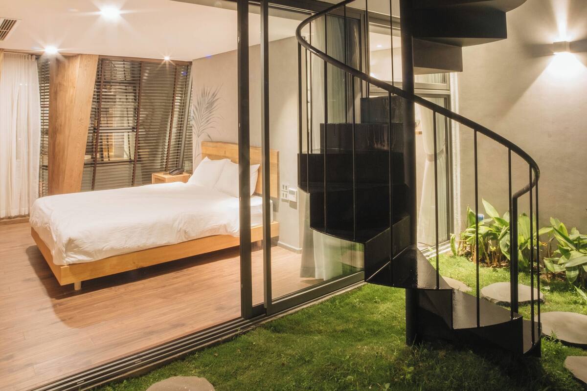 A modern bedroom with a glass-enclosed staircase, a bed, and a view of the outdoors.