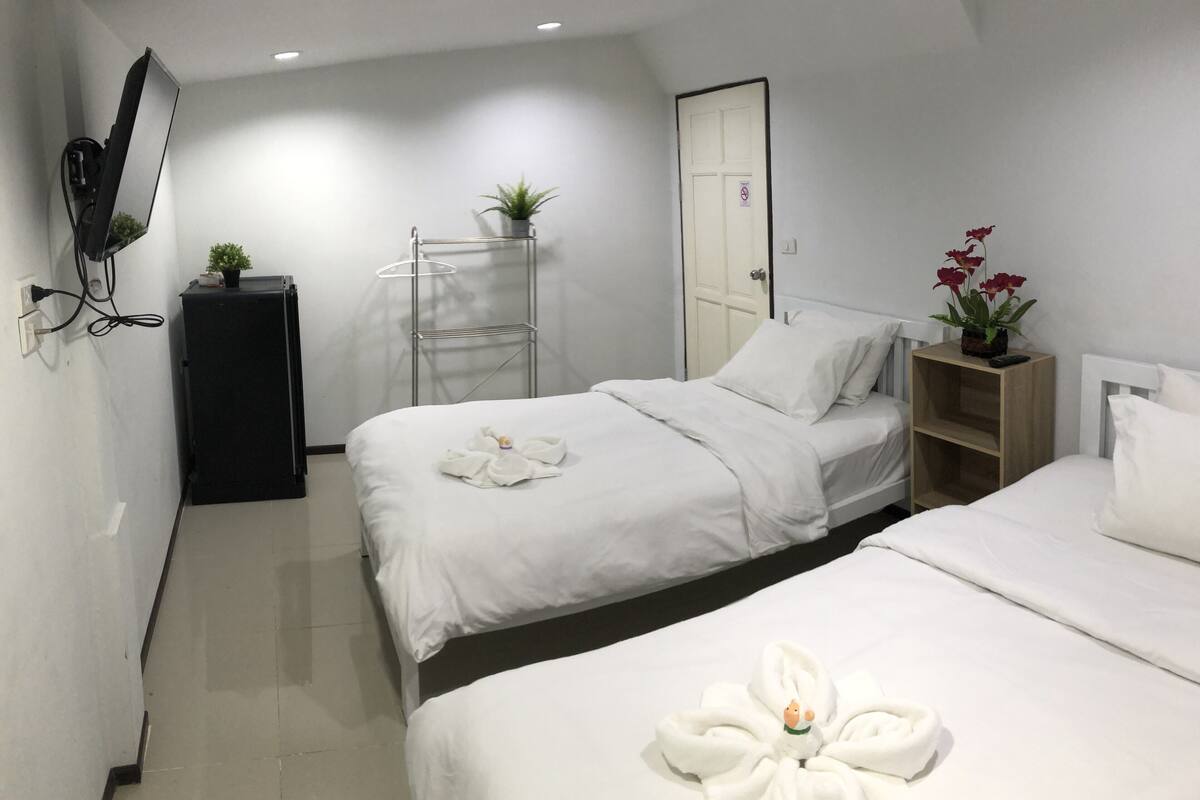 A hotel room with two beds, a wardrobe, a mirror, a plant, and a towel art display.