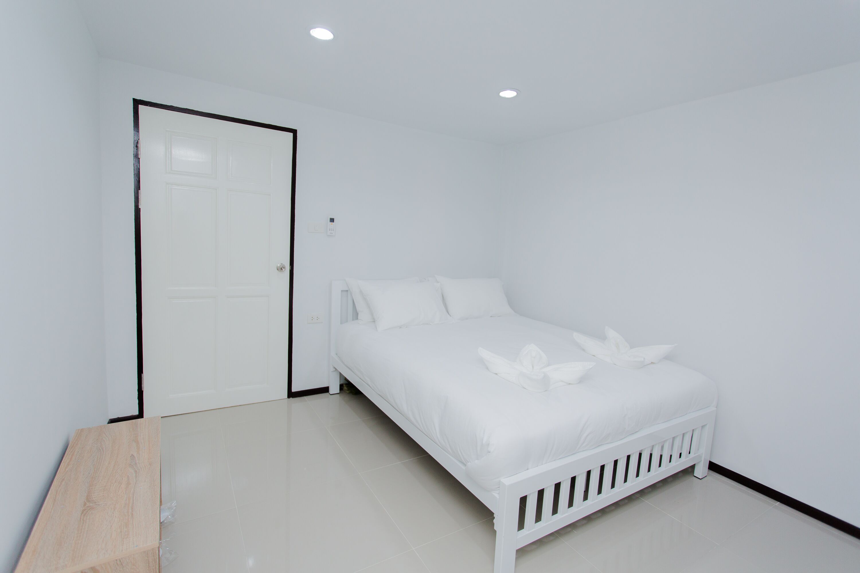 A white bedroom with a bed, a door, and a wooden bench.