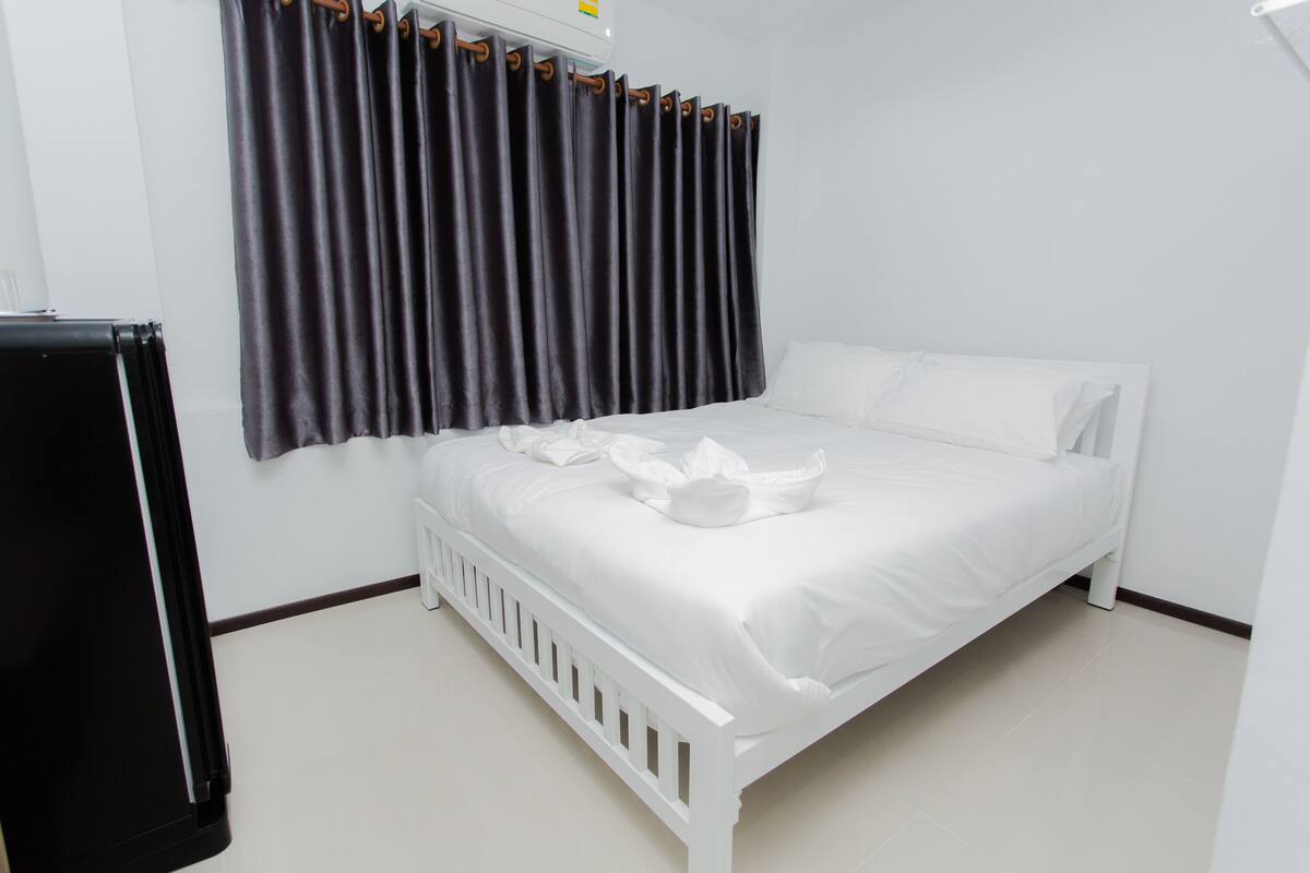 A white bed with a white headboard, a dark curtain, and a white wall.