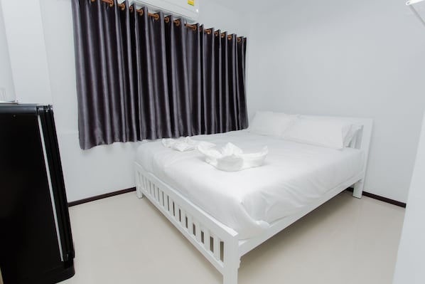 Un lit blanc avec une tête de lit blanche, un rideau foncé et un mur blanc.