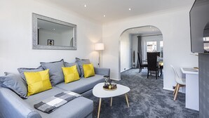Een moderne woonkamer met een grijze bank, gele kussens, een witte salontafel en een grote spiegel aan de muur.