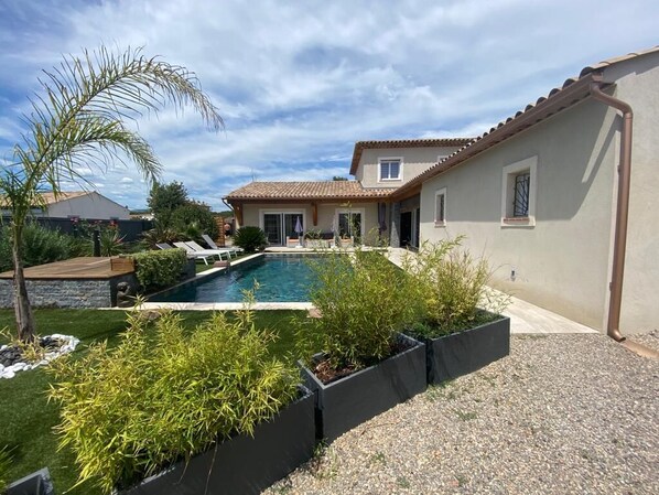 A residential property with a swimming pool, a patio area, and a garden with various plants.