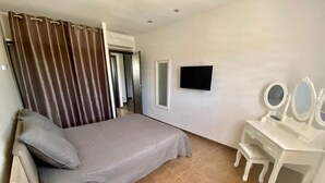 Un dormitorio con cama, televisor, tocador con espejos y cortina.