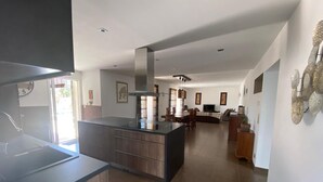 Una cocina moderna con una isla central, un comedor con sofá y televisor, y una sala de estar con chimenea.