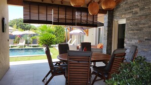 Un patio cubierto con piscina, mobiliario exterior y un muro de piedra.