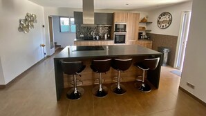 Una cocina moderna con una isla central, taburetes de bar, electrodomésticos de acero inoxidable y un elemento decorativo en la pared.
