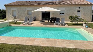 A swimming pool with lounge chairs and a table under a patio umbrella.