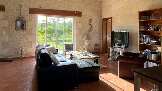 A spacious living room with a stone wall, a large window, a leather sofa, a coffee table, a bookshelf, and a television.