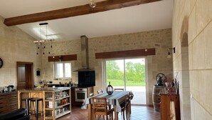 A spacious kitchen with a dining area, wooden beams, and a view of greenery outside.