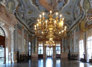 A grand hall with a large chandelier, ornate ceiling, and classical architecture.