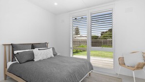 Ein Schlafzimmer mit einem Bett, einem Sessel und Blick ins Freie durch große Fenster.