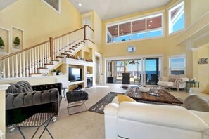 Relax in a spacious living area with a grand staircase, plush sofa, and wall-mounted TV.