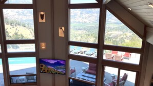 Ett rymligt vardagsrum med en stor TV, bekväma sittplatser och en vacker utsikt över bergen genom stora fönster.