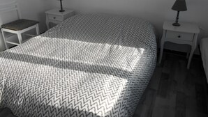 A bedroom with a patterned bedspread, two bedside tables with lamps, a chair, and a small table. - WATERFRONT APARTMENT (Jard-sur-Mer)