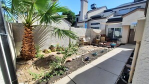 Un patio trasero con una palmera, un pequeño jardín y una zona de patio con mobiliario exterior.