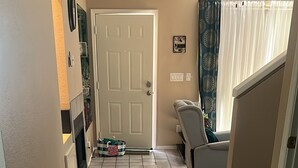 Un pasillo con suelo de madera, una puerta, un pequeño tapete y una silla.