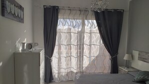 Een slaapkamer met een bed, een nachtkastje met een lamp, een kapstok en een raam met gordijnen.