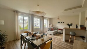 Un salon moderne avec un coin repas, de grandes fenêtres et une vue sur le quartier.