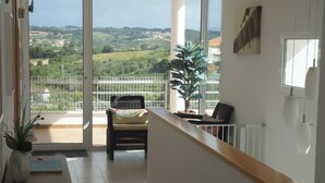 A balcony with a view of a green landscape, a wicker chair, a potted plant, and a small table with a book and a vase. - 3 Bedroom villa with swimming pool in quiet village with countryside views (Alcobaca)