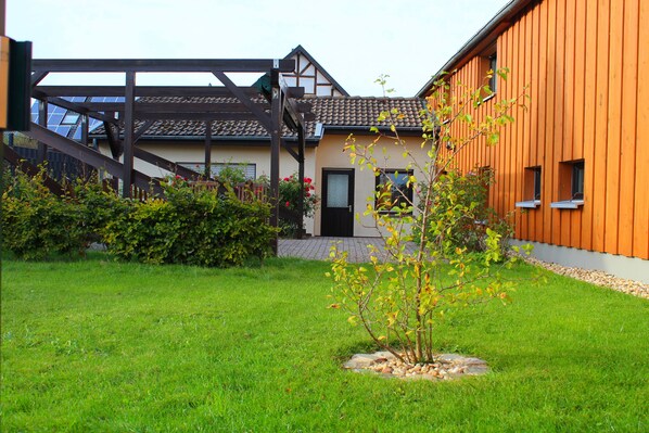 A modern building with a wooden facade, a visible entrance, and a well-maintained lawn with a small tree.