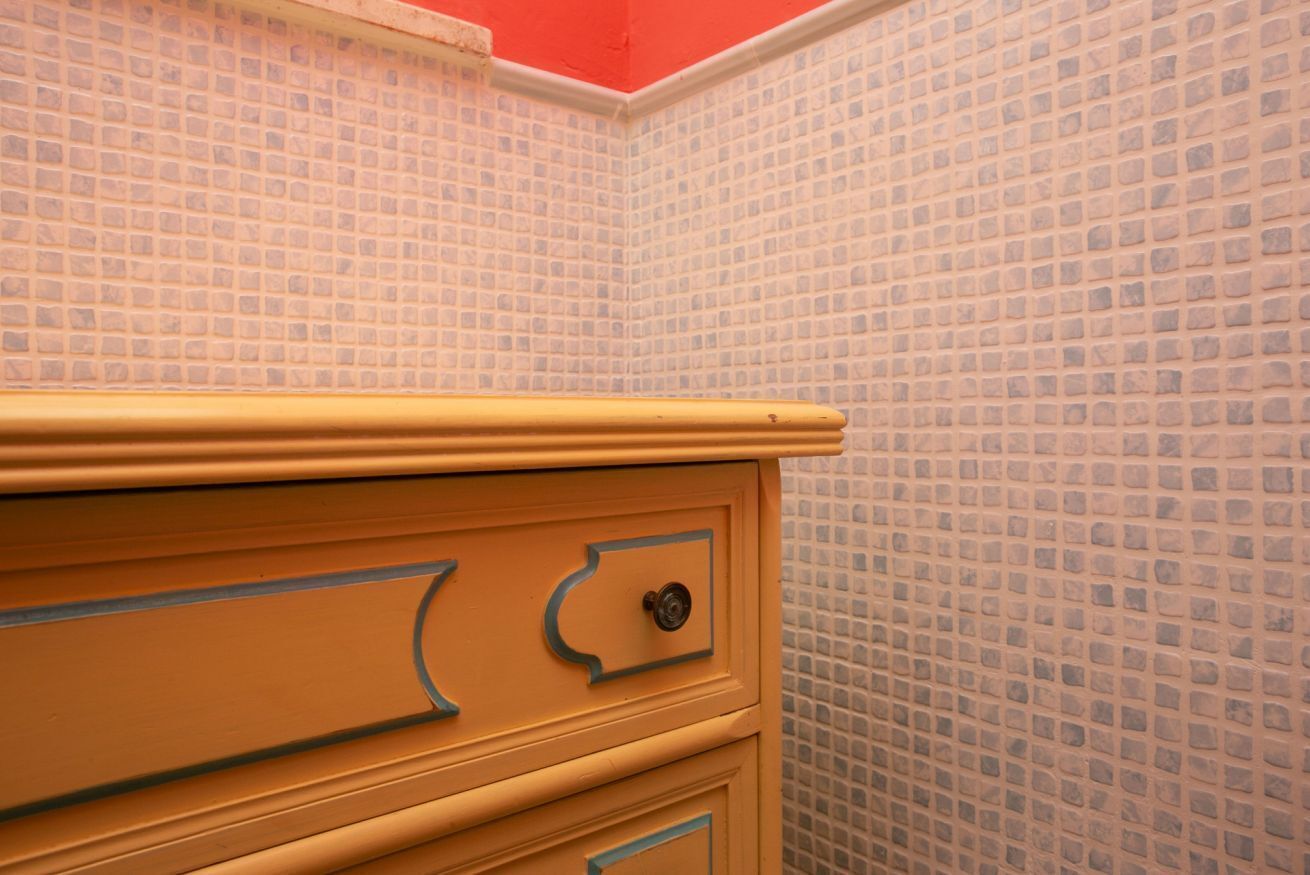 A bathroom with a tiled wall and a yellow vanity with drawers.