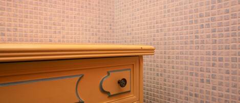 A bathroom with a tiled wall and a yellow vanity with drawers.