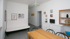 Een gezellig, ruimtelijk ingericht vertrek met een bank, een houten eettafel, een televisie op een kast en fotolijstjes aan de wanden.