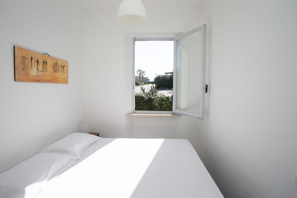 Ein Einzelbett in einem Zimmer mit Fenster, einem Wandbild und einer weißen Deckenleuchte.