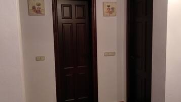 Un pasillo con dos puertas de madera oscura, paredes blancas y suelo de baldosas.