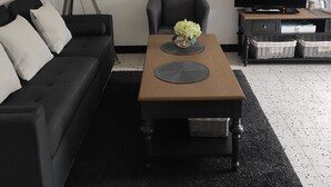 En moderne stue med en sort sofa, et træsofabord med en vase blomster, en gulvlampe, et fjernsyn og et billede i ramme på væggen.