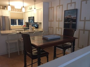 Cozinha moderna com armários brancos, forno embutido e área de jantar com mesa e cadeiras de madeira.