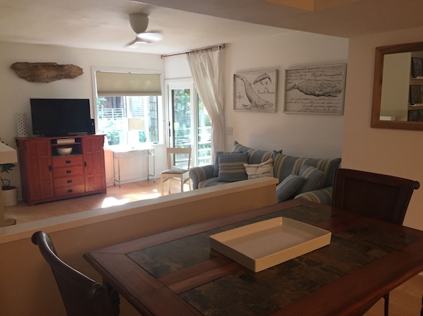A living room with a wooden dining table, a sofa, a TV on a cabinet, and a window with curtains.
