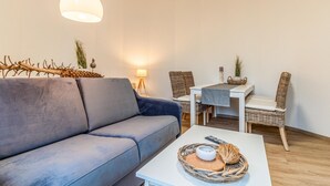 A modern living room with a grey sofa, a white coffee table with a woven basket, wicker chairs, and a small dining table. - Gorgeous home in Otterndorf with WiFi (Otterndorf)