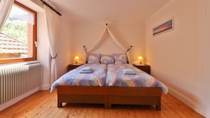 A bedroom with a wooden bed, white curtains, a window with a view, and two bedside lamps. - Maison Balboa gîtes for 2 to 12 people (Sondernach)