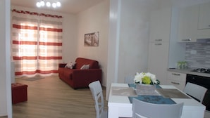 Una sala de estar moderna con un sofá rojo, una mesa de comedor con sillas blancas y una cocina con gabinetes blancos y una estufa a gas.