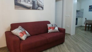 Un sofá rojo con cojines estampados en una habitación con suelo de madera y una puerta blanca.