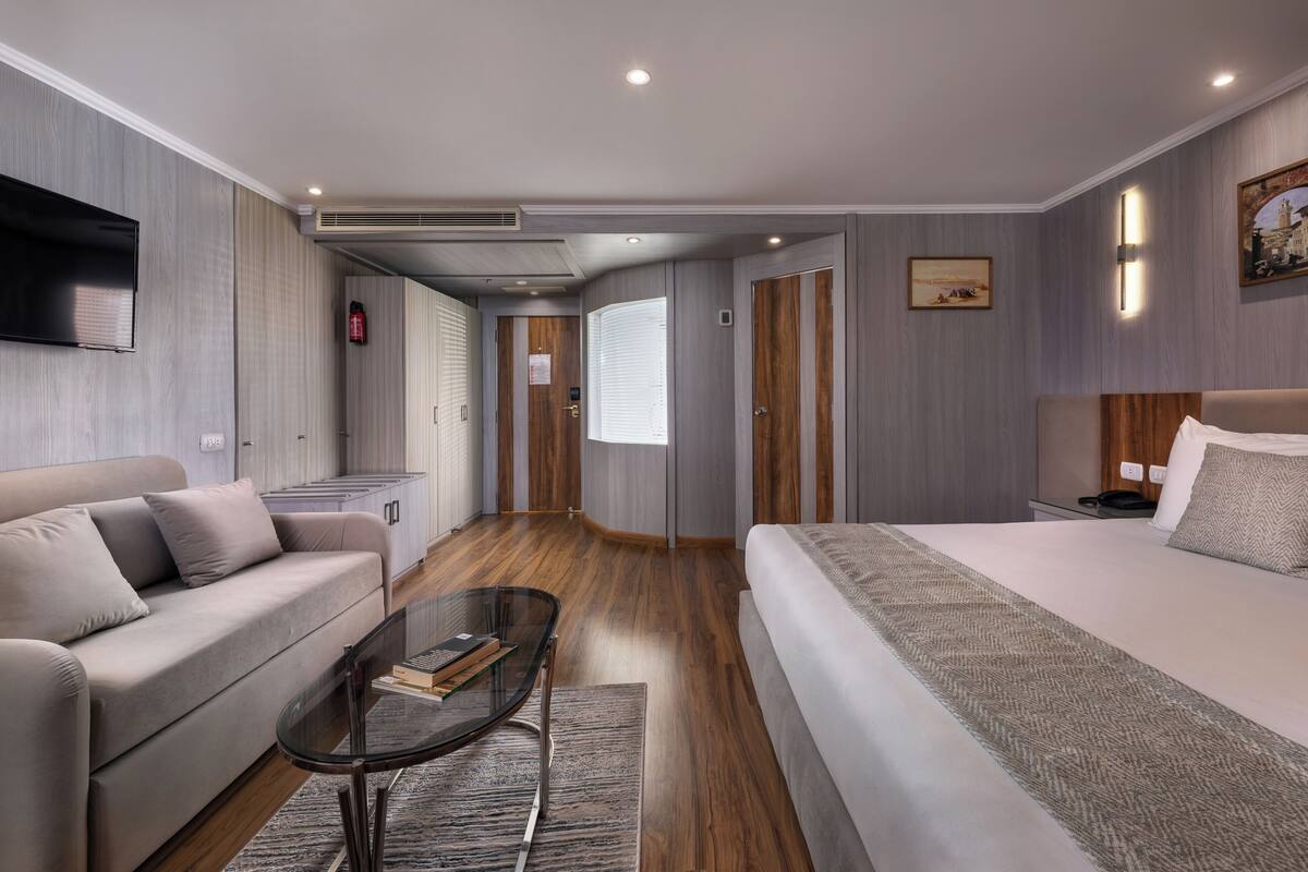 Habitació d'hotel moderna amb un sofà, un llit, una taula de cafè de vidre i una televisió.