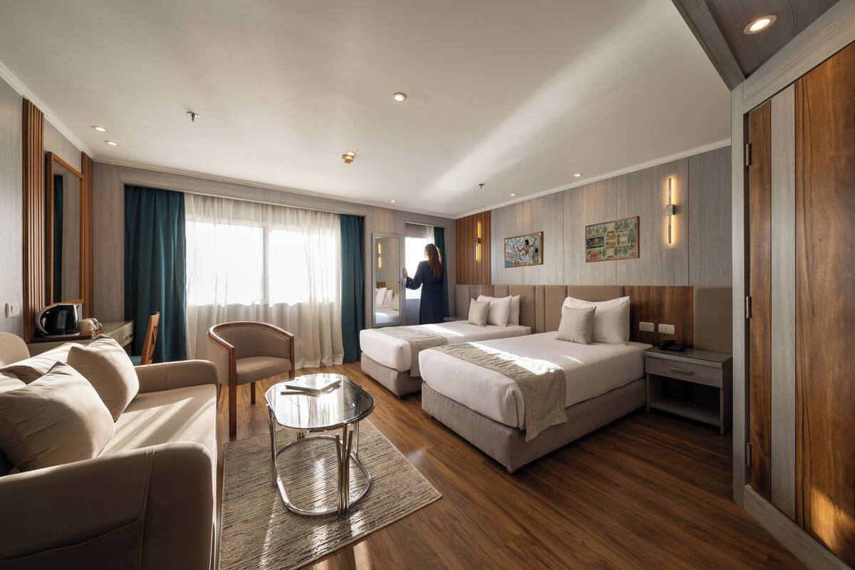 Habitació d'hotel amb un sofà, dos llits, una taula petita i un mirall.