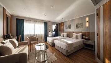 A hotel room with a sofa, two beds, a small table, and a mirror.